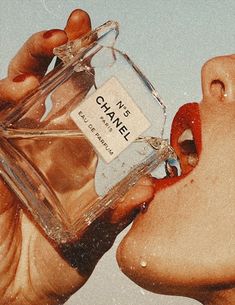 a person holding a bottle of chanel perfume in their mouth to smell it with its tongue out