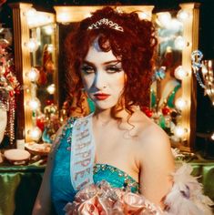 a woman with red hair wearing a tiara in front of a mirror and christmas decorations