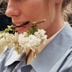 a woman holding flowers in her mouth and looking at the camera while wearing a blue shirt