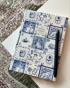 a notebook with blue and white tiles on it sitting on top of a table next to a pen