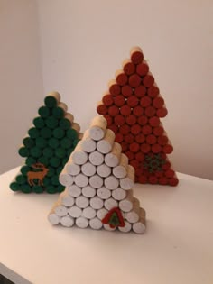 three christmas trees made out of wine corks on a white counter top, each decorated in different shapes and sizes