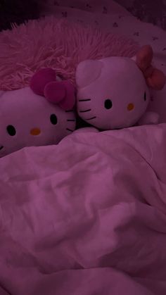 two hello kitty stuffed animals laying on a bed