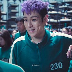 a man with purple hair standing in front of other people wearing green and white jackets