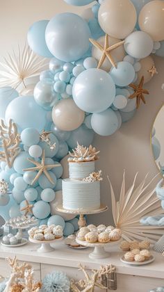 a table topped with lots of blue and white balloons, starfishs and cake