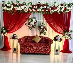 a red couch sitting in front of a white and red wall with flowers on it