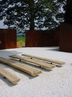 three wooden benches sitting on top of a white gravel covered ground next to metal sculptures