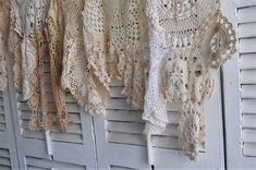 several crocheted shawls hanging on the side of a white building with shutters