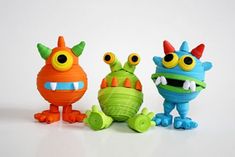 three toy monsters sitting next to each other on a white surface with one looking at the camera