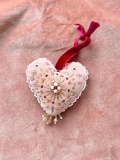 a pink heart shaped ornament hanging from a red ribbon on a pink cloth