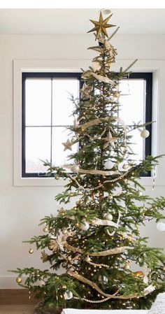 a christmas tree with gold stars and ornaments on it in front of a large window