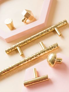 three different types of gold jewelry on pink and white surface with framed objects in background