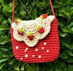 a crocheted red purse hanging from a tree with green leaves in the background