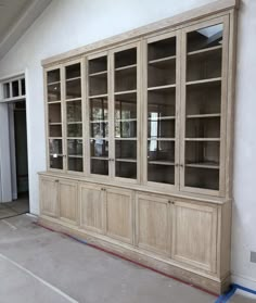 a large wooden bookcase with glass doors on the front and side walls in an empty room