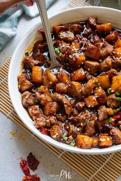 a bowl filled with meat and vegetables on top of a bamboo mat next to a spoon