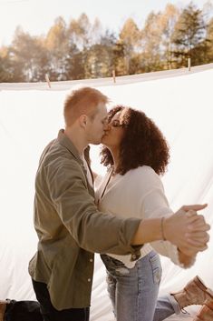 a man and woman standing next to each other near a white sheet covered wall with trees in the background