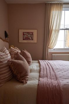 a bed with pink sheets and pillows next to a window