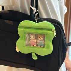 two teddy bears in a green frame on a black bag with a person holding it