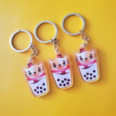 three keychains with cats on them sitting next to each other in front of a yellow background