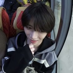 a young man is sitting on a bus looking at the camera while wearing a black and grey jacket