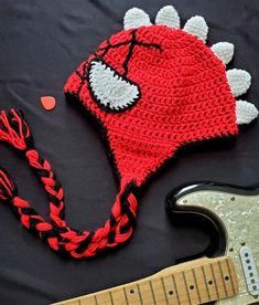 a crocheted hat and guitar string on a black sheet with a red electric guitar