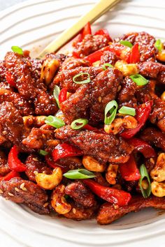 a white plate topped with meat covered in sauce and green onions next to a wooden spoon