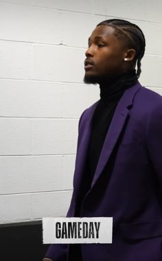 a man in a purple suit standing next to a white wall with the word gameday on it