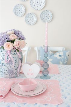 the table is set with pink and blue flowers in vases, plates, and napkins