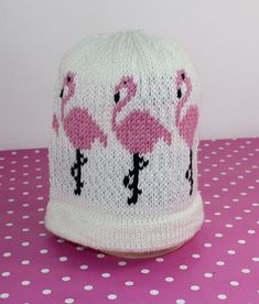 a knitted hat with pink flamingos on it sitting on a polka dot table