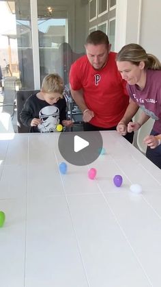 a man and two children are playing with balls on the table while an adult watches