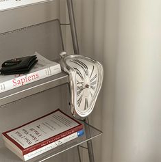 a stack of books sitting on top of a metal shelf next to a wall mounted clock