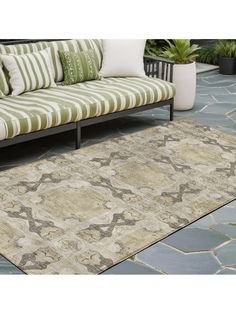 an outdoor area rug with green and white striped pillows on the ground next to a couch