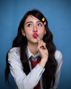 a woman with long black hair wearing a tie and holding a stick in her mouth