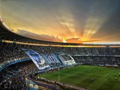 the sun is setting over a soccer stadium with many people on the field and fans in the stands