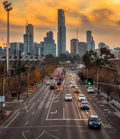 cars are driving down an empty street in front of the cityscape at sunset