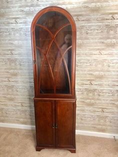 a wooden china cabinet with glass doors on the top and bottom shelves, in front of a wallpapered background