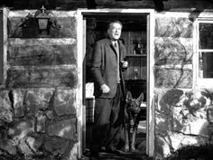 an old photo of a man and his dog in front of a stone house with the door open