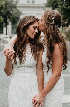 two women in white dresses kissing each other