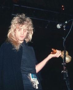 a woman standing in front of a microphone holding a donut and looking at the camera