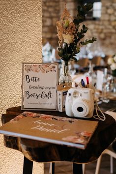 a table topped with a camera next to a vase filled with flowers and writing on it