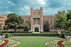 a large building with many trees and bushes in front of it on a cloudy day