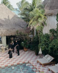 two men in tuxedos are standing near a pool and thatched roof huts