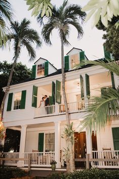 a white house with green shutters and palm trees