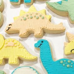 decorated cookies in the shape of dinosaurs on a white tablecloth with blue and yellow icing