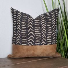 a brown and black pillow sitting on top of a wooden table next to a plant