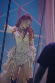 a woman with red hair wearing a white corset and black boots standing next to a pole