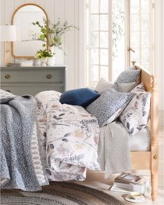 a bed with blue and white comforters in a room next to a dresser, mirror and window