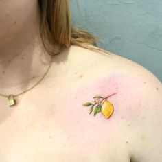 a woman's chest with a small tattoo of a lemon and leaves on it