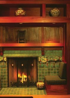 a fireplace in a room with green tiles and wooden shelves above it is lit by candles