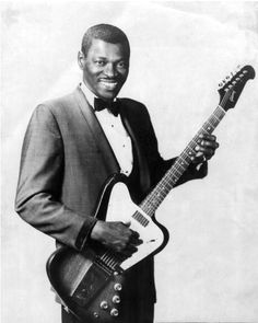 a black and white photo of a man in a suit holding an electric bass guitar