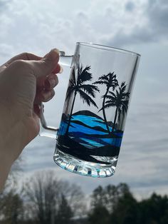 a person holding up a glass with water and palm trees on it